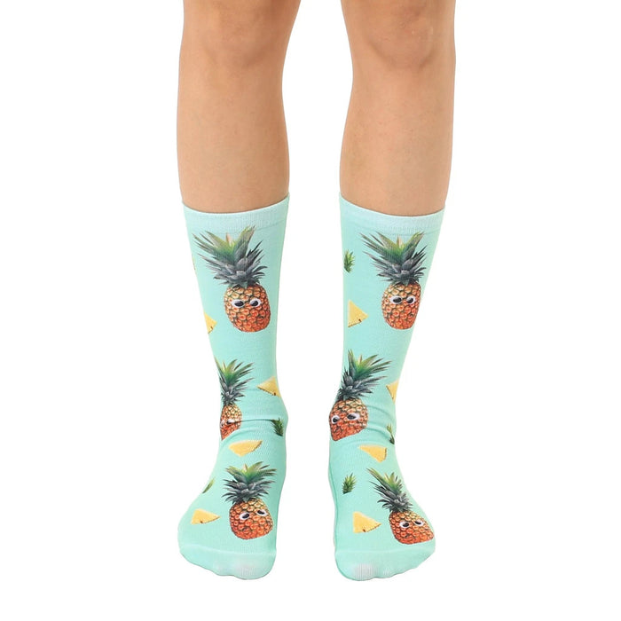 A pair of mint green crew socks with a fun all-over print of googly-eyed pineapples and pineapple wedges.