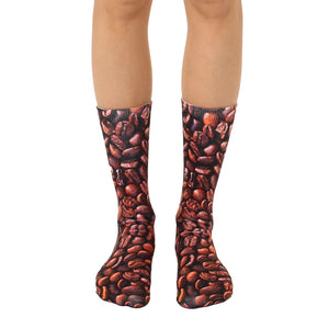 A pair of brown crew socks with an all-over print of coffee beans. Shown on a model's legs.