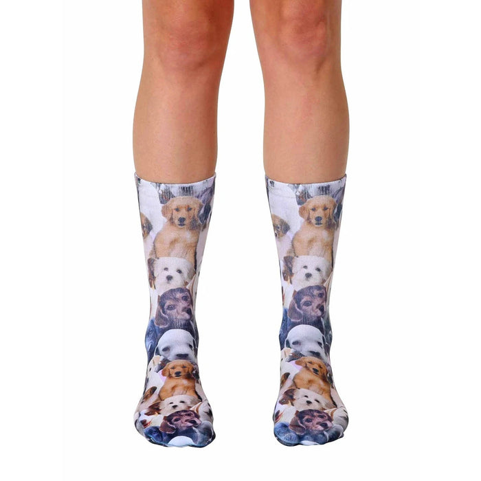 A pair of crew socks covered in an all-over print of adorable puppies in various breeds and colors. The socks are mainly white with brown, tan, and black puppies.