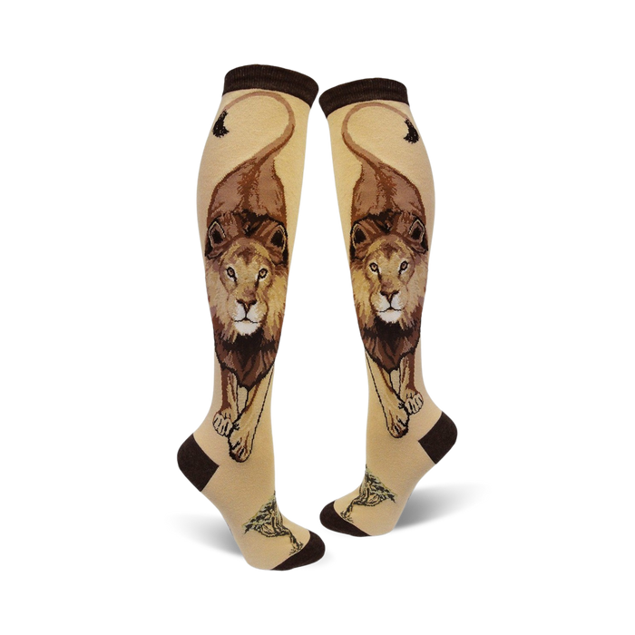 Pair of cream knee-high socks with a detailed brown lion design, including its mane and tail, and small tree accents at the bottom. }}