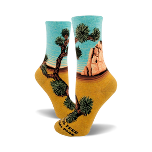 A pair of women's crew socks showcasing a Joshua Tree National Park design. The socks are teal and mustard yellow, depicting a desert landscape with iconic Joshua trees and rock formations.