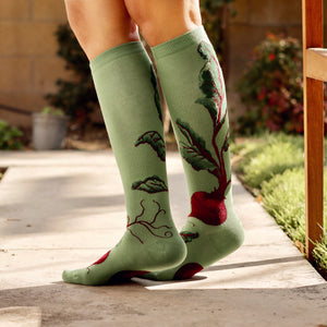 Lifestyle shot of a woman sitting on a wooden bench wearing the beet socks.