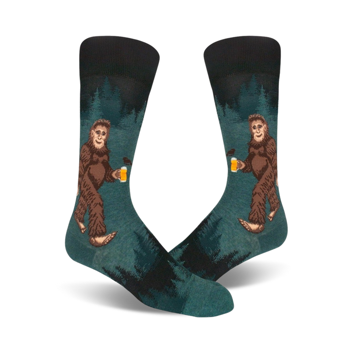 Pair of teal crew socks depicting a Bigfoot character enjoying a beer in a forest setting. Darker teal and black accents.