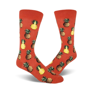 Pair of crew socks with orange background and repeated pineapple pattern. Pineapples are yellow and brown.