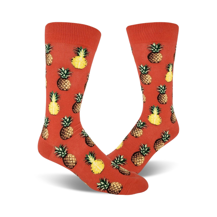 Pair of crew socks with orange background and repeated pineapple pattern. Pineapples are yellow and brown.