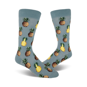 Close up view of a pair of blue crew socks with a repeated pineapple pattern. Pineapples are yellow and brown.