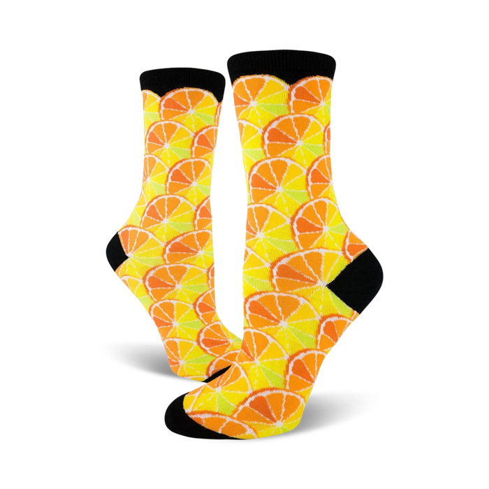 Pair of crew socks with a citrus fruit pattern.  Oranges and lemons in yellow, orange, and pale green on a white background. Black cuffs.