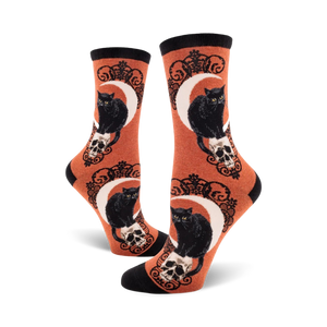 Crew socks in orange and purple featuring black cats perched on skulls beneath a crescent moon. Ornate detailing.