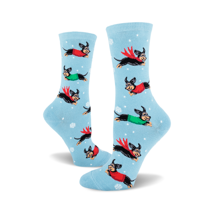 pair of women's crew socks, sky blue background, featuring dachshunds in winter sweaters and scarves leaping through snowflakes. front view. }}