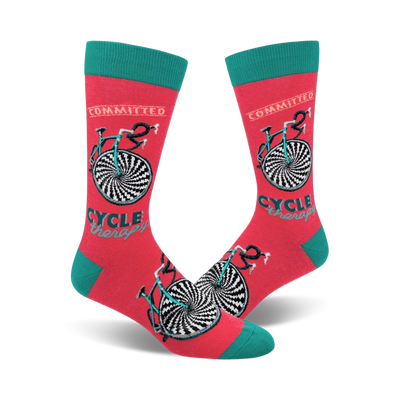 A pair of coral crew socks with a teal cuff. The socks feature a black and white hypnotic bicycle design and the words 'Cycle Therapy' and 'Committed'.