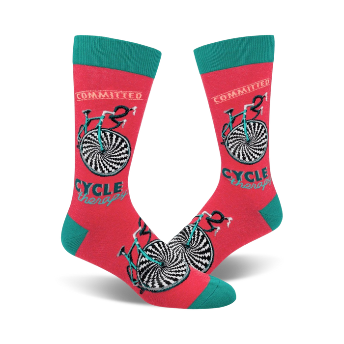 A pair of coral crew socks with a teal cuff. The socks feature a black and white hypnotic bicycle design and the words 'Cycle Therapy' and 'Committed'. }}