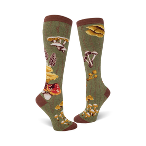 Close-up view of a pair of knee-high socks in olive green, showcasing the detailed mushroom illustrations and wood-grain background.