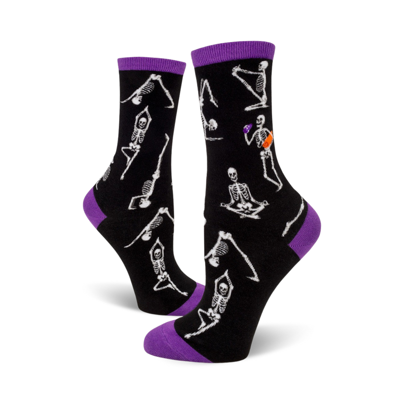 A pair of black crew socks with purple cuffs. The socks are adorned with a pattern of white skeletons performing yoga poses.