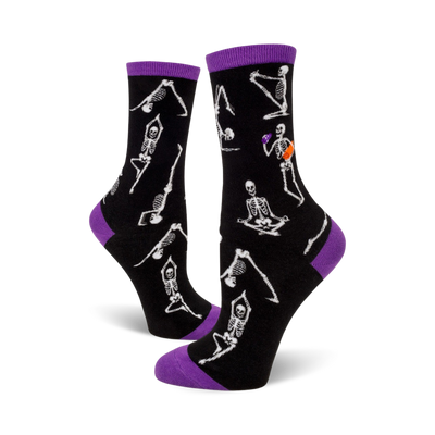 A pair of black crew socks with purple cuffs. The socks are adorned with a pattern of white skeletons performing yoga poses.