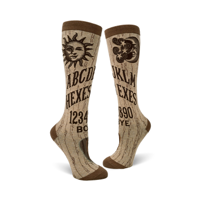 A pair of beige knee-high socks with a brown Ouija board design. The socks feature a sun, moon, and alphabet graphics.
