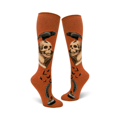 Pair of rust-colored knee-high socks. Design includes a raven perched on a skull above an antique book, quill pen, inkwell, and flying birds.