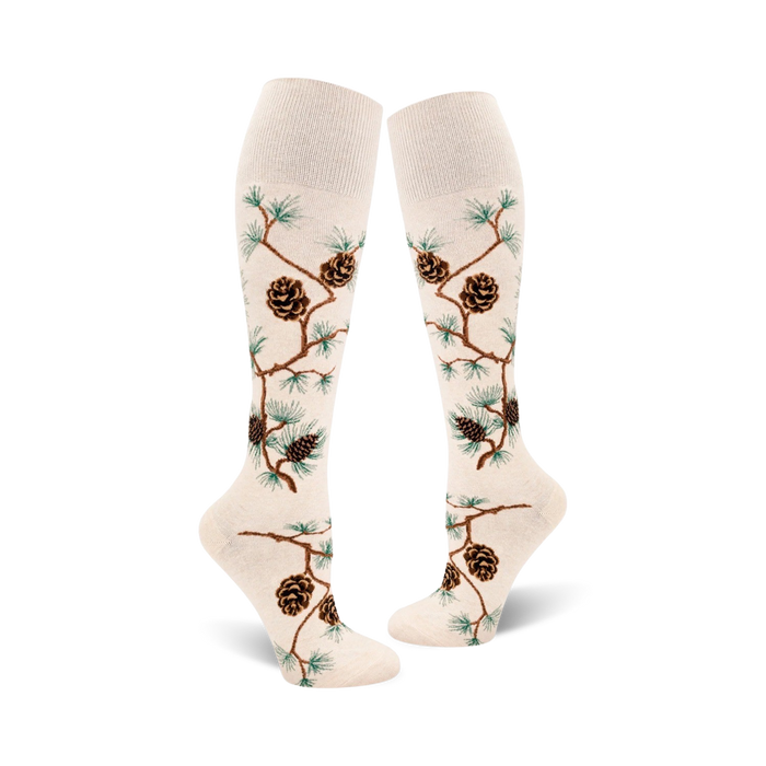 Pair of off-white knee-high socks with brown pine cones and green pine branches artfully arranged on the fabric. }}