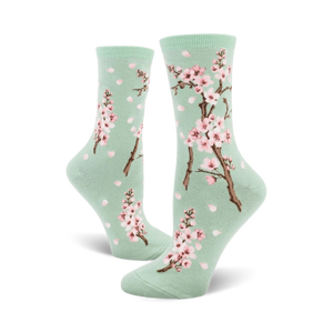 Pair of crew socks with a pastel green background, pink cherry blossoms, and falling petals design.