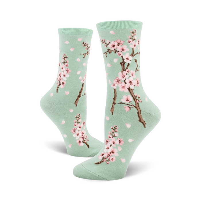 Pair of crew socks with a pastel green background, pink cherry blossoms, and falling petals design.