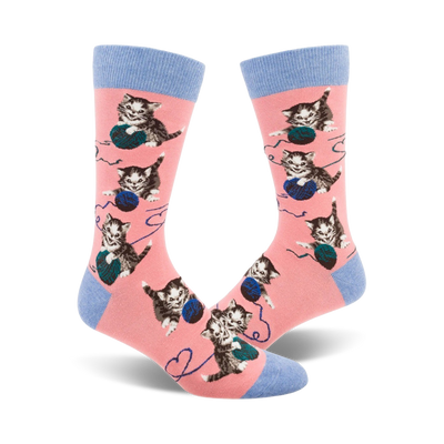 Pair of pink crew socks featuring repeated images of kittens batting at balls of yarn.  Socks have light blue cuffs.