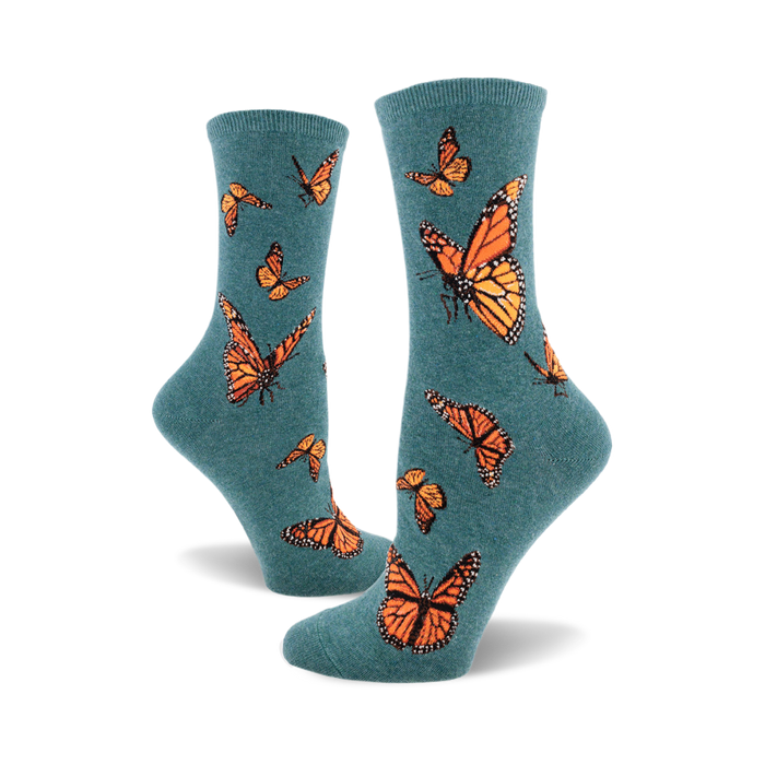 A pair of teal crew socks featuring a pattern of orange monarch butterflies. The socks are shown from the side, showcasing the design. }}