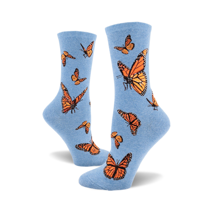 A pair of light blue crew socks adorned with a pattern of orange monarch butterflies. The socks are shown from the side, one sock partially obscuring the other. }}