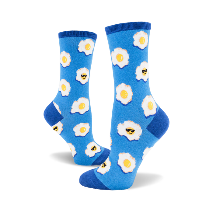 A pair of women's crew socks in blue with a pattern of fried eggs wearing sunglasses. Yellow yolks and white egg whites stand out on the vibrant blue background. }}