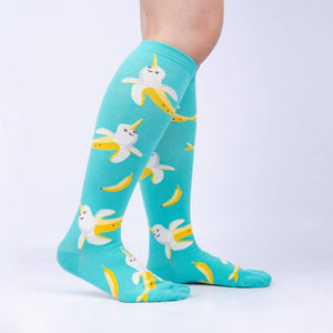 A pair of blue knee-high socks with a pattern of yellow bananas with narwhal faces.