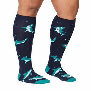 A pair of knee-high compression socks in dark blue with a pattern of cartoon sharks in teal.