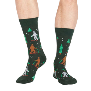 Lifestyle shot showing the 'Ready, Yeti, Go!' socks on a person's legs.  The socks are dark green with a festive pattern.