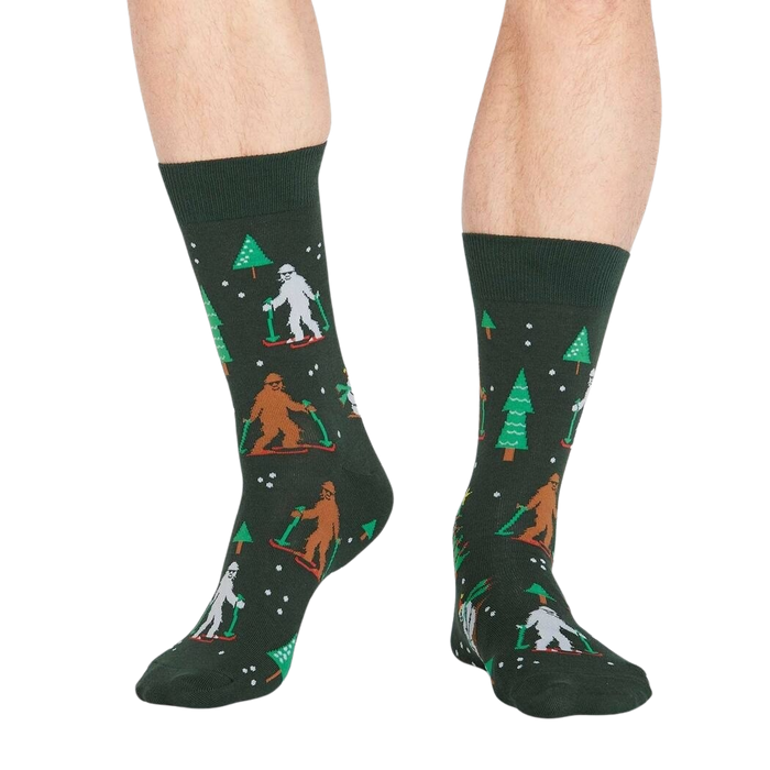 Lifestyle shot showing the 'Ready, Yeti, Go!' socks on a person's legs.  The socks are dark green with a festive pattern.