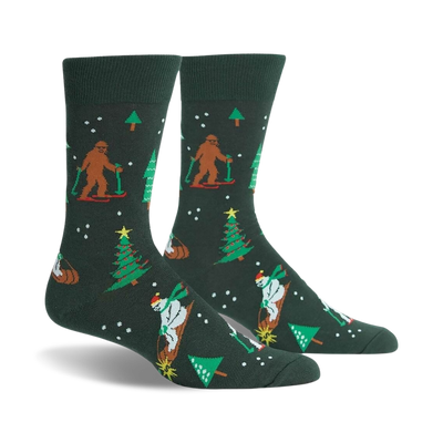 A pair of dark green crew socks with a whimsical Christmas design. Features Bigfoot characters skiing, snowmen, and Christmas trees.