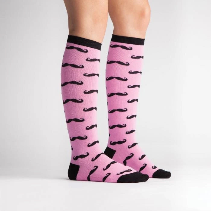 Lifestyle shot showing the Mustache knee-high socks on a person's legs. Pink and black pattern.