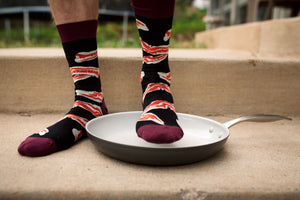 Lifestyle shot of a person's legs wearing the bacon socks near a frying pan.