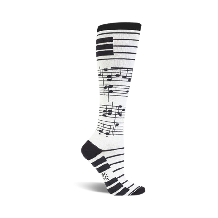 A pair of white knee-high socks with black musical notes and a piano keyboard cuff design. }}