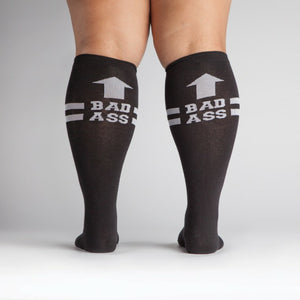 Flat lay product shot: Two black 'Bad Ass' knee-high socks laid flat.