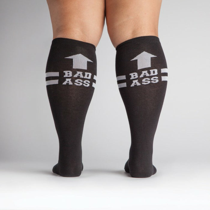 Flat lay product shot: Two black 'Bad Ass' knee-high socks laid flat.
