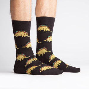 Lifestyle photo showing Tacosaurus socks on a person's feet. The socks are black with a fun taco-dinosaur pattern.