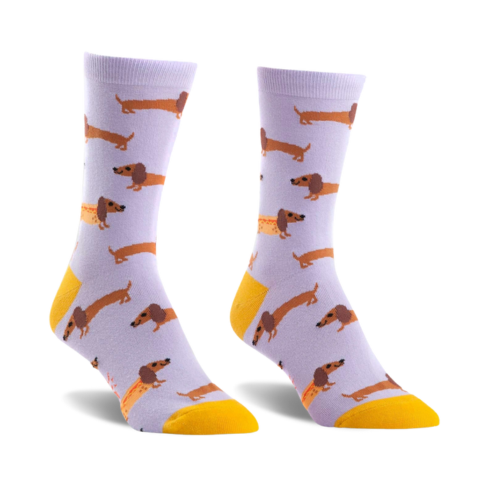 Pair of lavender crew socks featuring a repeating pattern of brown dachshunds and one dachshund shaped like a hot dog. Yellow accents at the cuffs. }}
