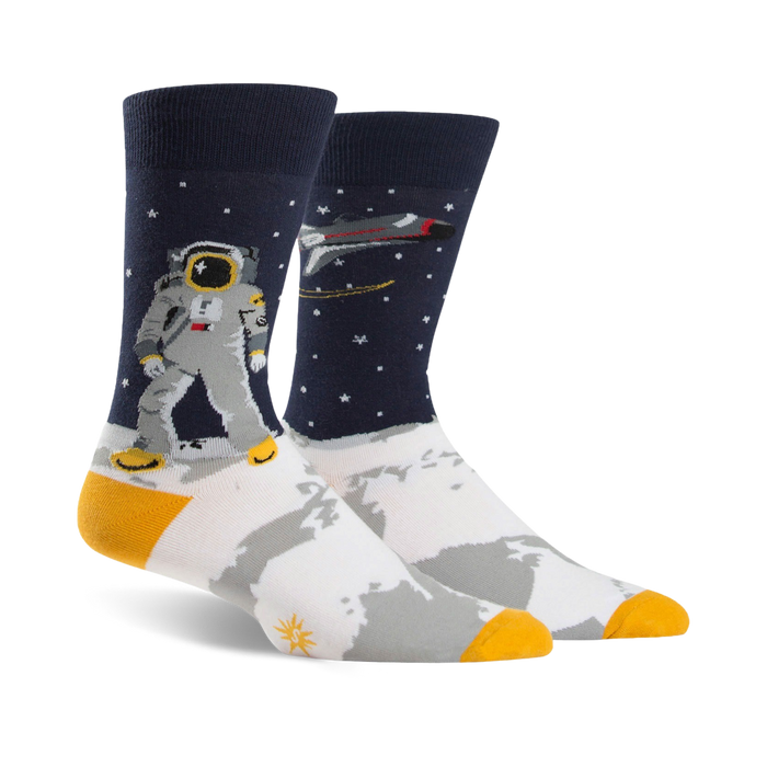 A pair of crew socks; navy blue background with white moon surface, astronaut, rocket, and gold accents. }}