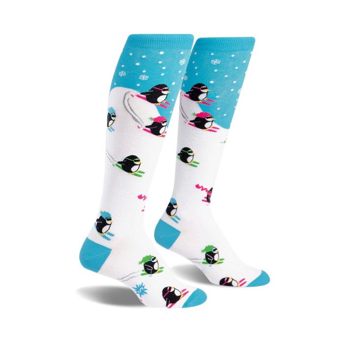 A pair of white knee-high socks with a playful design. Blue accents at the top and bottom. Penguins skiing in neon pink, green, and black are featured on a white background with light blue snowflake accents at the top. }}