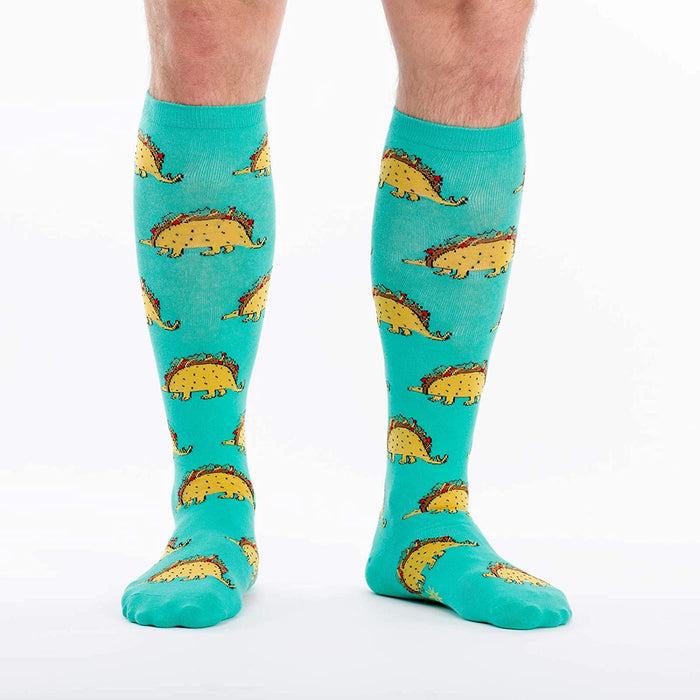 A pair of blue knee-high socks with an all-over pattern of cartoon tacos with dinosaur legs.