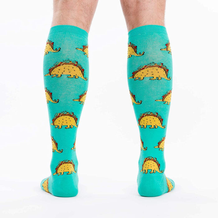 A pair of blue knee-high socks with an all-over pattern of cartoon tacos with dinosaur legs.