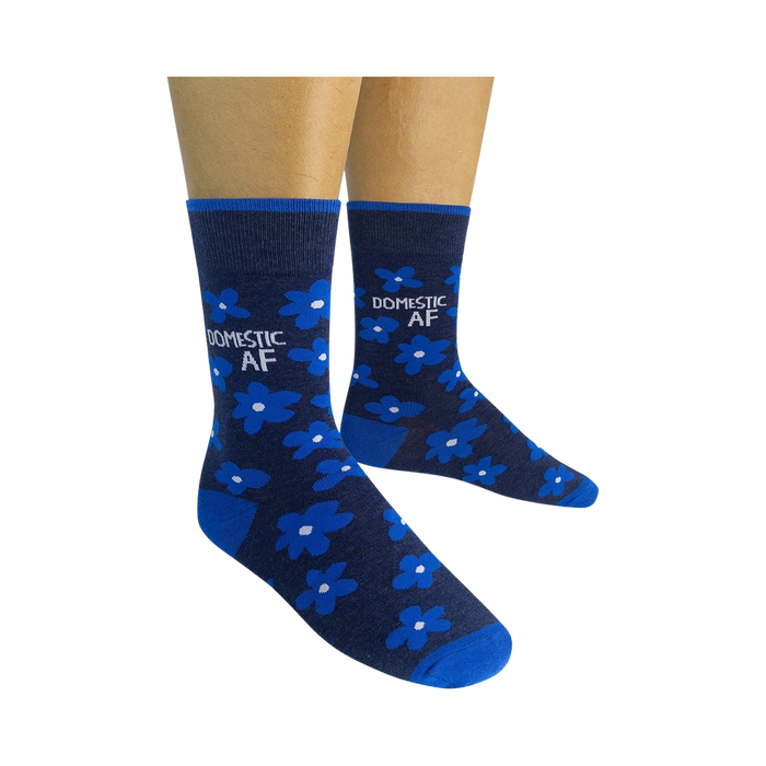 Pair of navy blue crew socks with bright blue flowers and 'DOMESTIC AF' text, shown on a model's feet.