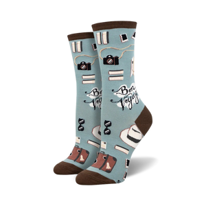 A pair of crew socks in teal and mint green, featuring cameras, books, hats, and suitcases; the phrase 'Bon Voyage' is printed on the socks.