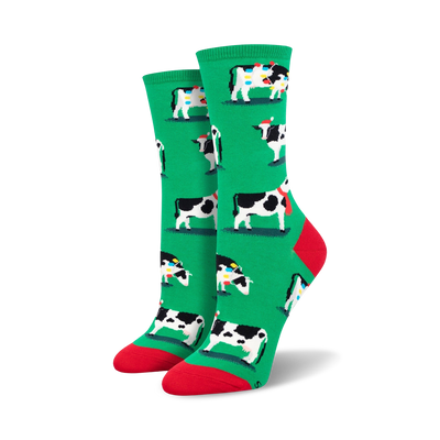 Pair of women's crew socks. Green background with a repeating pattern of black and white cows wearing Christmas hats and scarves.