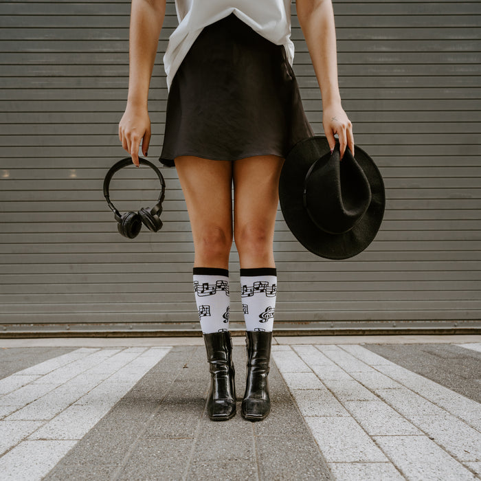 Lifestyle shot: Woman wearing white musical note socks and black boots.