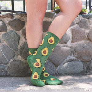 A person is sitting on a stone wall with their legs crossed. They are wearing green socks with a pattern of avocados on them.