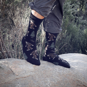 Lifestyle shot of a person wearing black Bigfoot socks; shows the socks with rolled-up pants in an outdoor setting.