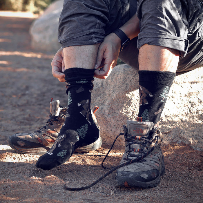 Close-up of a person putting on black Bigfoot socks; shows detail of the sock's design and texture.